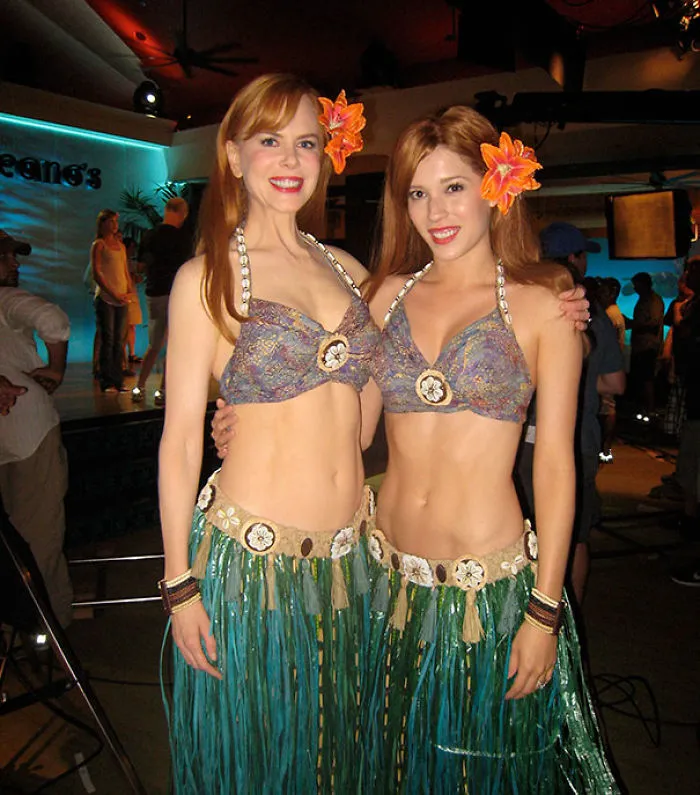 Two women dressed as Hawaiian dancers showcasing Hollywood celebrities body doubles in a studio setting.