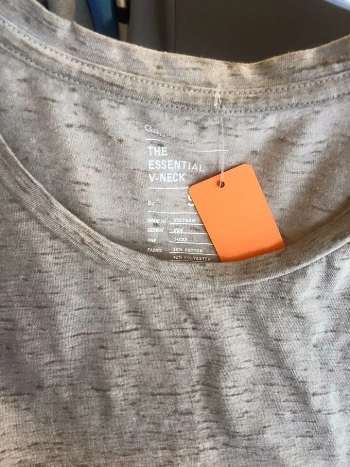 A V-neck shirt with "THE ESSENTIAL V-NECK" label, featuring a hang tag that mistakenly obstructs the view.