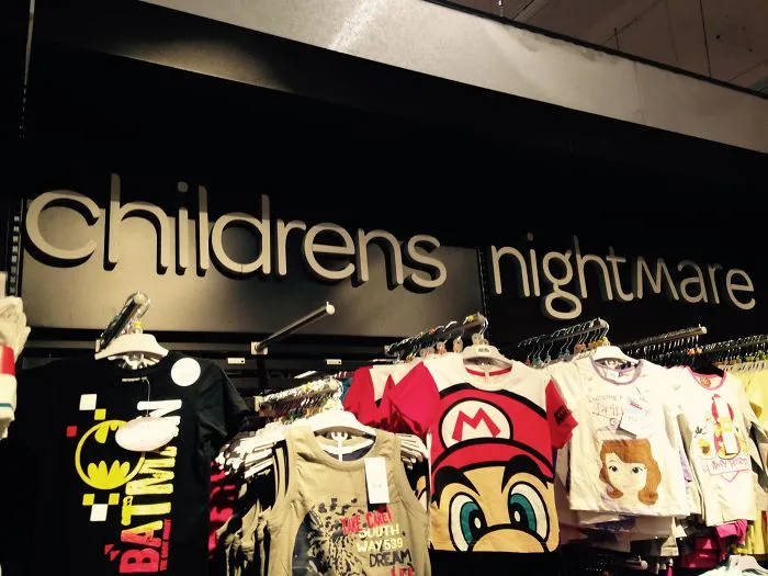 Store sign reads "childrens nightmare" instead of "children's nightwear," overlooking a rack of kids' clothing.