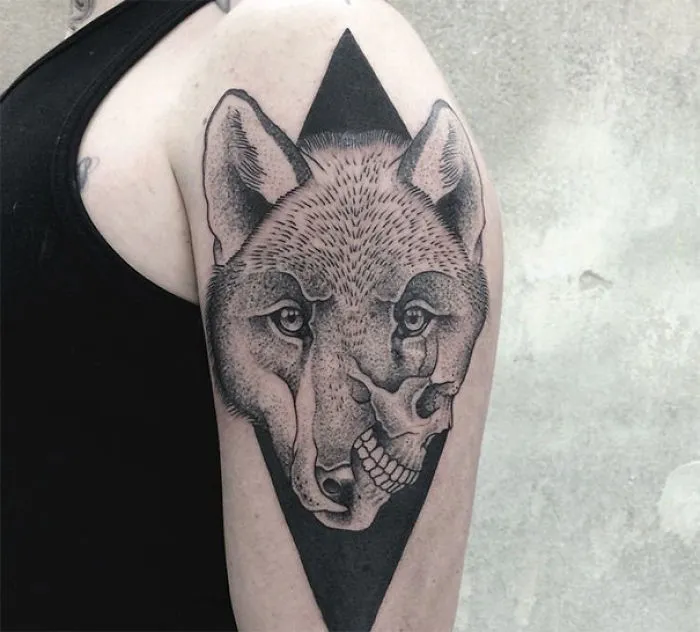 Symmetrical tattoo of a wolf merging with a skull, designed with geometric elements on an upper arm.