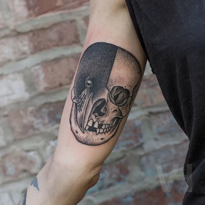 Symmetrical tattoo by Valentin Hirsch, blending a skull with a bird, showcasing nature and geometry on an arm.
