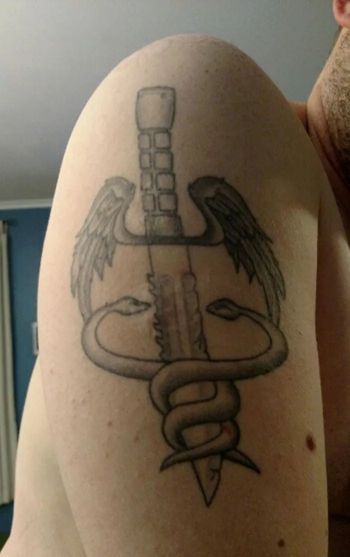 Sword and wings scar-covering tattoo on upper arm with intertwined snakes.