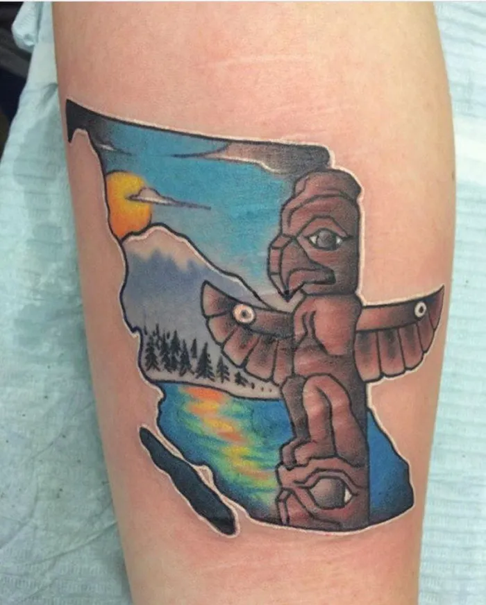 Totem tattoo covering scar, featuring a landscape with mountains, forest, and sunset.