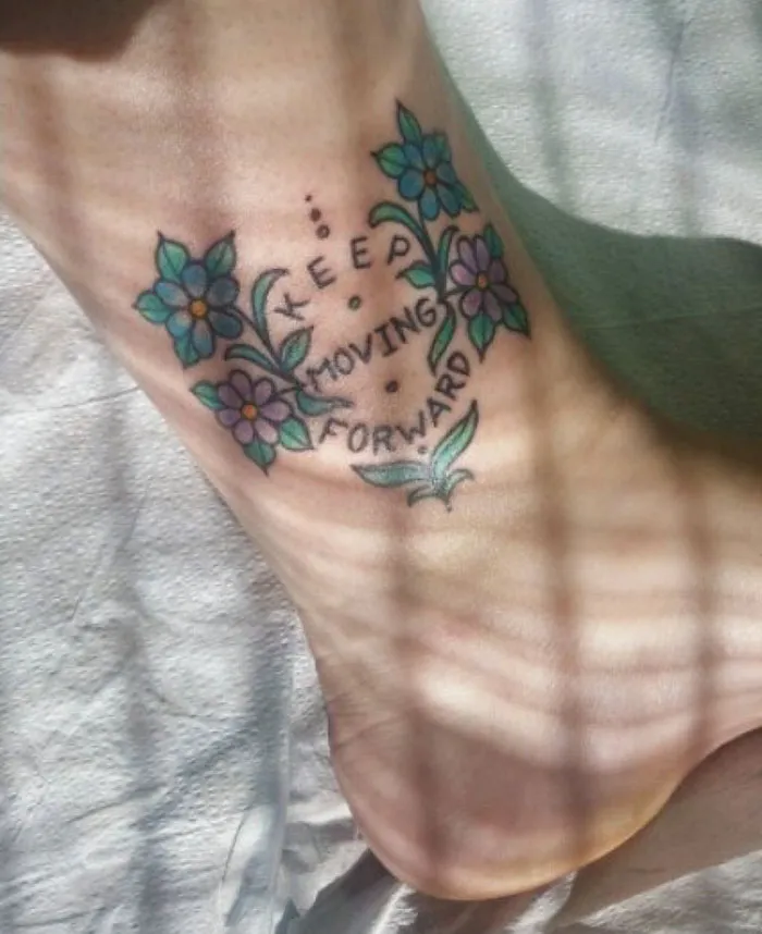 Tattoo with flowers and "Keep Moving Forward" design, covering a scar on the foot.
