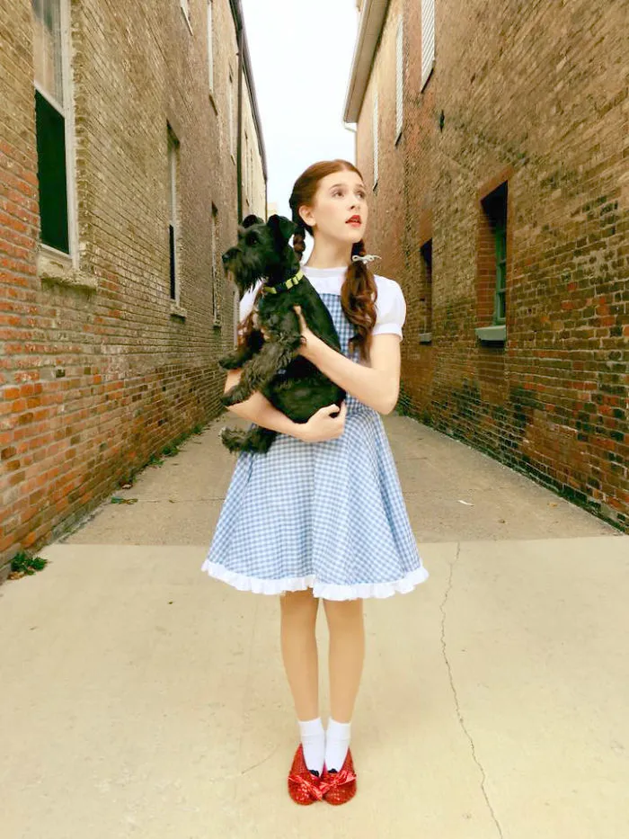 A girl dressed as Dorothy holding a small black dog as one of the creative Halloween costume ideas