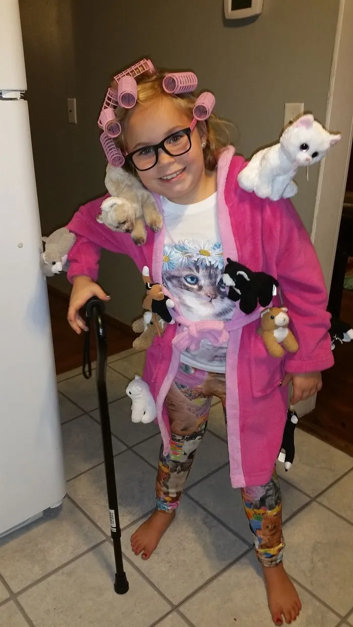 A young girl wearing a cat lady creative Halloween costume with hair curlers and plush cats