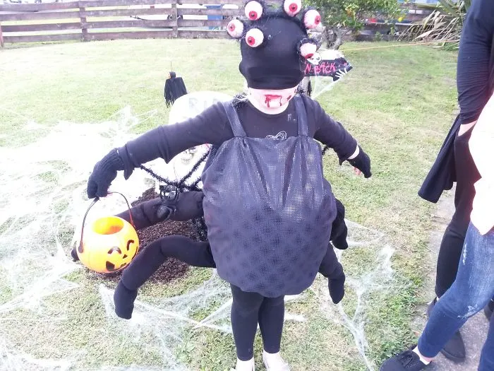 A child in a spider outfit holding a pumpkin bucket as creative Halloween costume ideas
