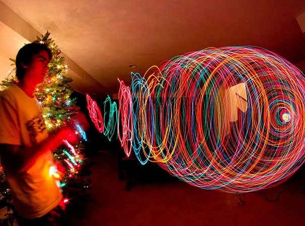 A man uses lights to create colorful patterns, showcasing photography as a creative illusion.