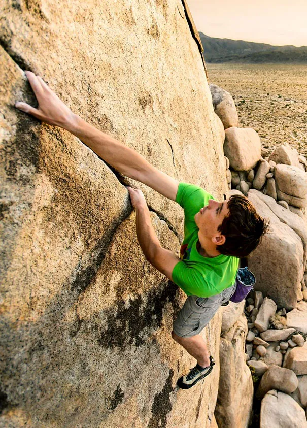 Climber in a green shirt scaling a rock face, showcasing photography illusions in outdoor settings.