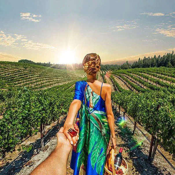 Woman in a blue dress holding a hand in a vineyard at sunset, capturing the essence of photography as illusion.