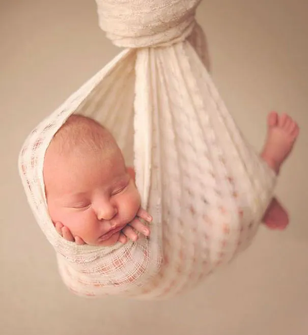A newborn baby gently hanging in a soft white wrap, illustrating how photography can create imaginative scenes.