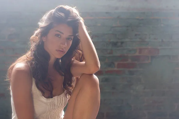 Woman posing in soft light against a textured wall, exemplifying photography as the biggest lie.