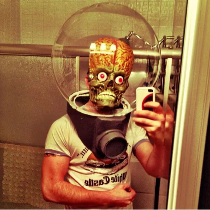 Man wearing a Mars Attacks alien mask in a bathroom for a creative Halloween costume idea