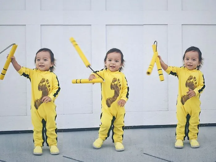 A toddler in a yellow jumpsuit holding nunchucks, inspired by Bruce Lee for creative Halloween costume ideas.