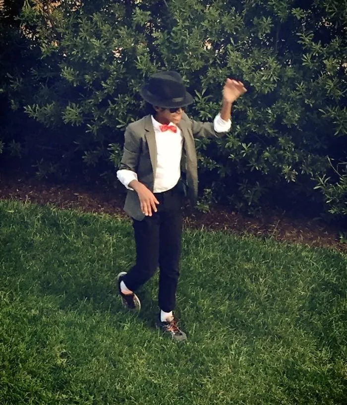 A young boy dressed in a suit and hat posing in a yard as creative Halloween costume ideas
