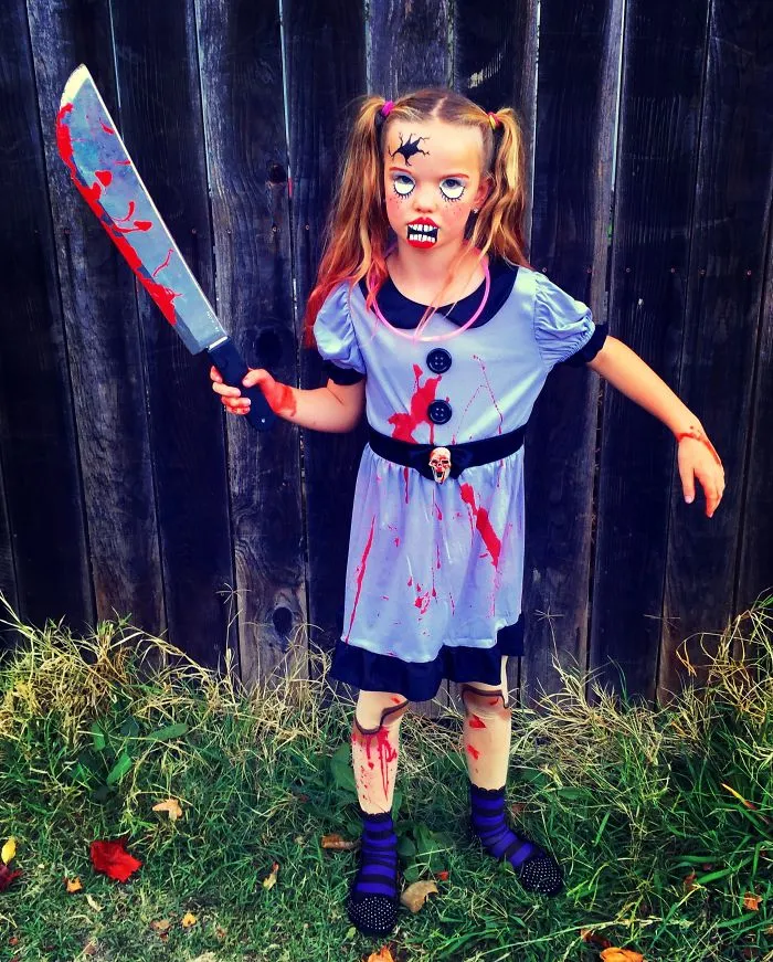 A young girl dressed as a spooky, bloody doll with a prop knife for creative Halloween costume ideas.