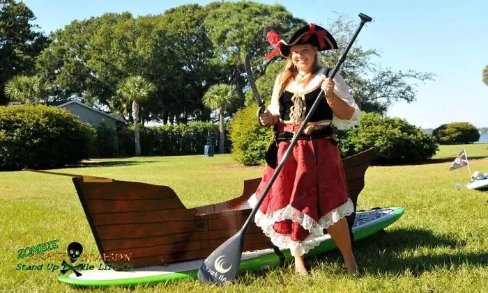 Woman in pirate attire standing on a paddleboard decorated as a ship for creative Halloween costume ideas.