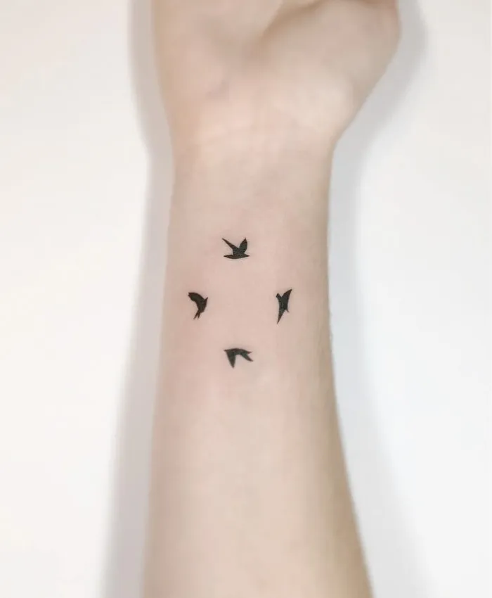 Small bird tattoos on a wrist, showcasing elegant minimalist design.