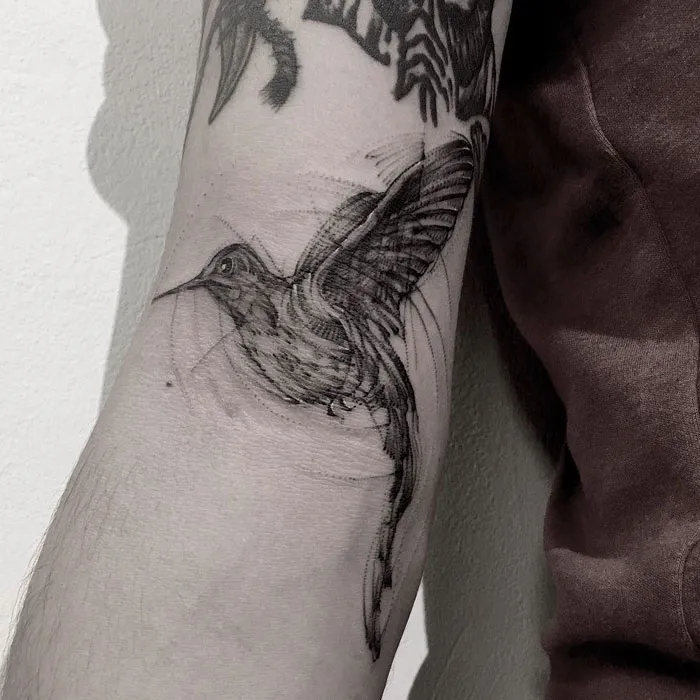Small bird tattoo on arm with intricate linework, showcasing a unique artistic design.