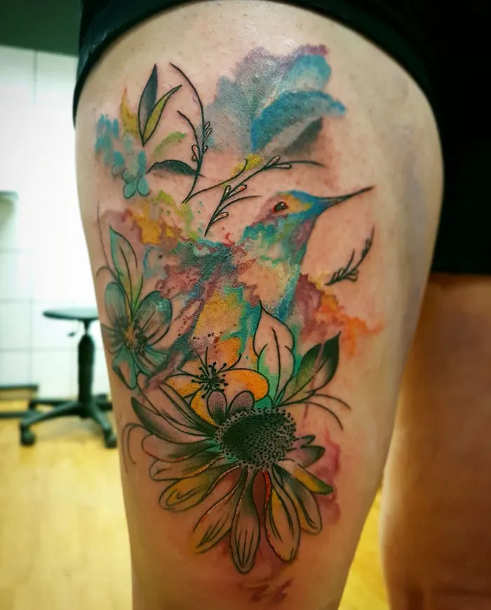 Colorful small bird tattoo with floral elements on the thigh.