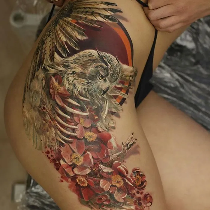 Close-up of a detailed small bird tattoo with floral elements on the thigh.