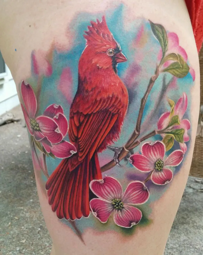 Unique small bird tattoo of a colorful red cardinal perched on a flowering branch with vibrant blossoms.