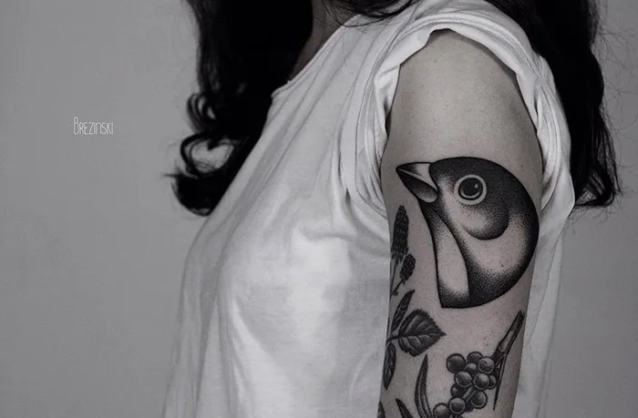 Woman with a unique small bird tattoo on her upper arm, featuring intricate details and shading.