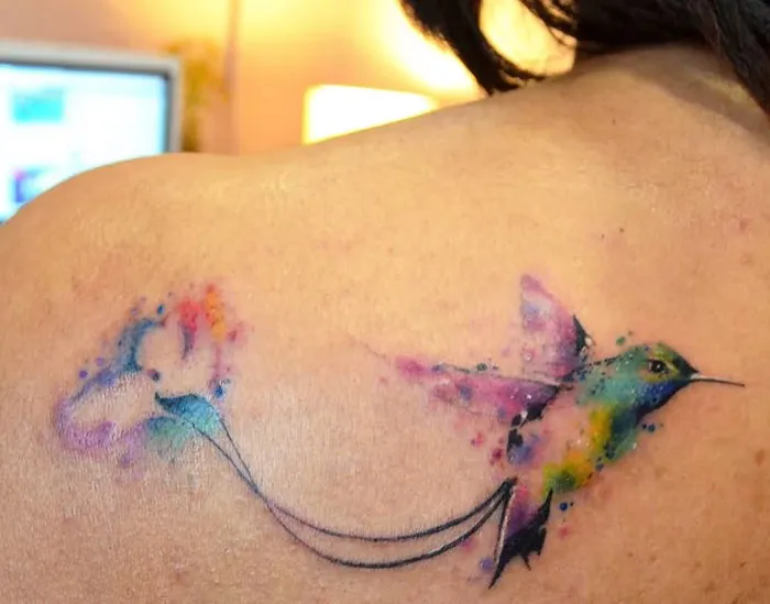 Colorful small bird tattoo on shoulder with watercolor effect.