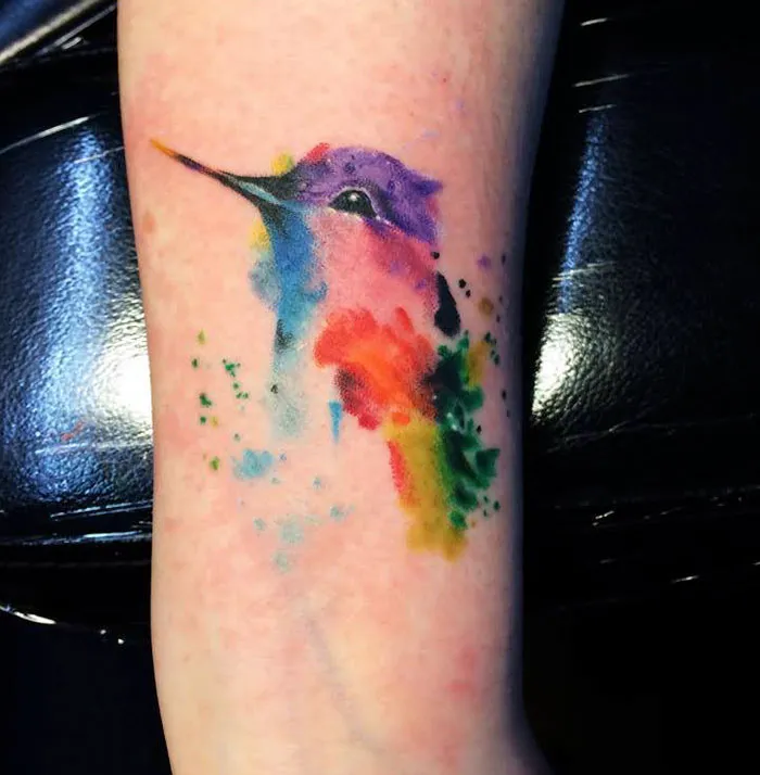 Watercolor small bird tattoo with vibrant colors on the arm.