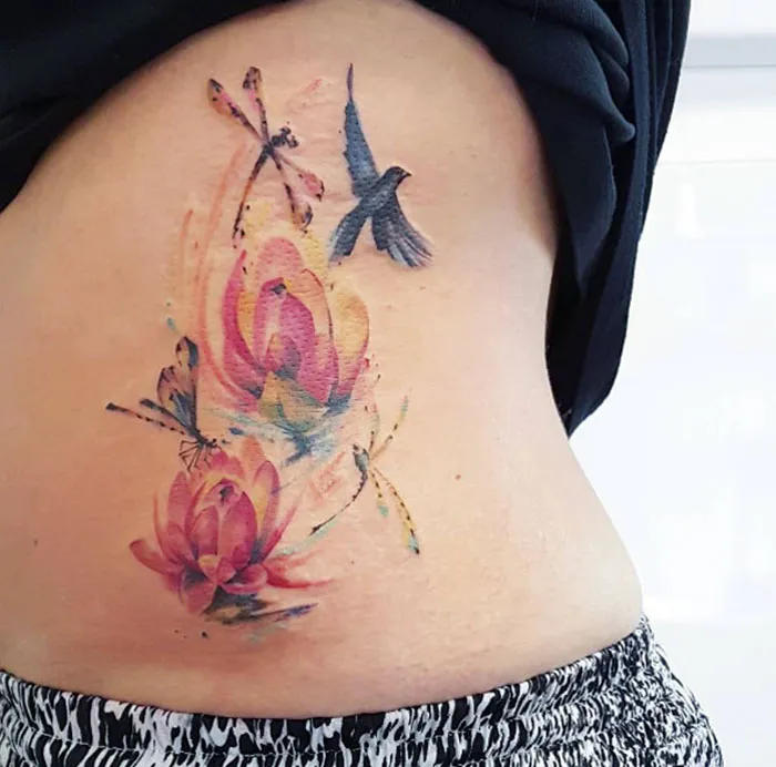 Colorful small bird tattoo with flowers on a person's side, showcasing unique ink design inspiration.
