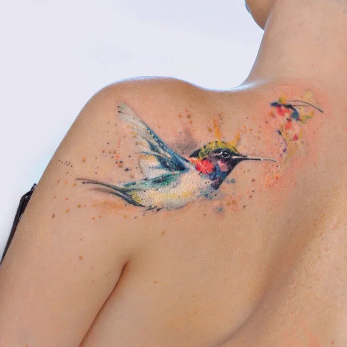 Colorful small bird tattoo on a shoulder, showcasing artistic detail and vibrant hues.