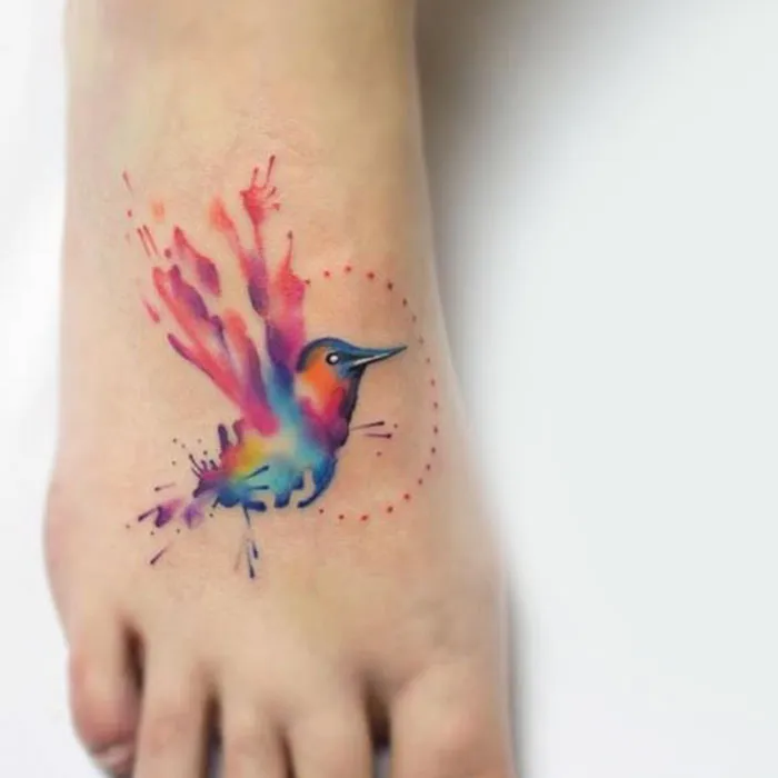 Colorful small bird tattoo with watercolor effect on foot.