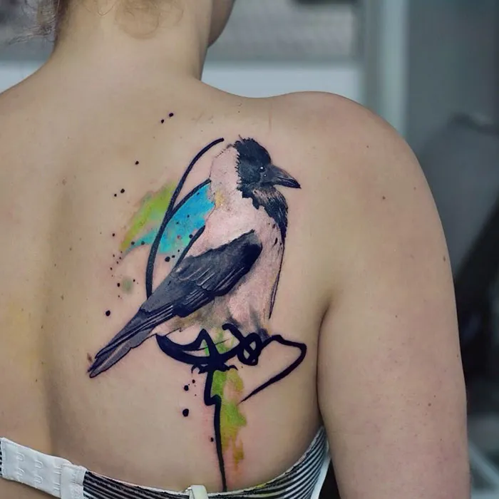 Colorful small bird tattoo on woman's back.