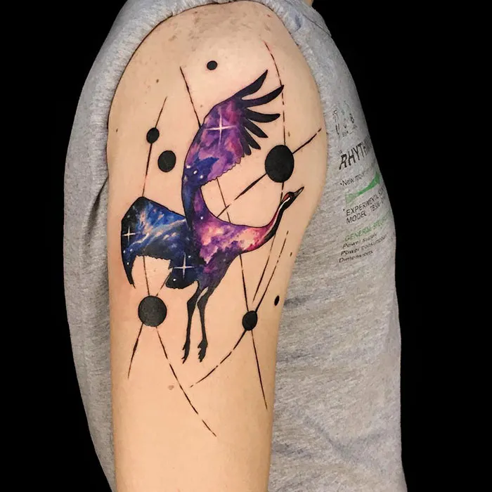 Cosmic small bird tattoo with purple galaxy design on upper arm.