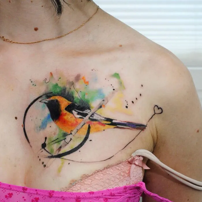Colorful small bird tattoo on shoulder, featuring artistic strokes and vibrant splashes, ideal for tattoo inspiration.