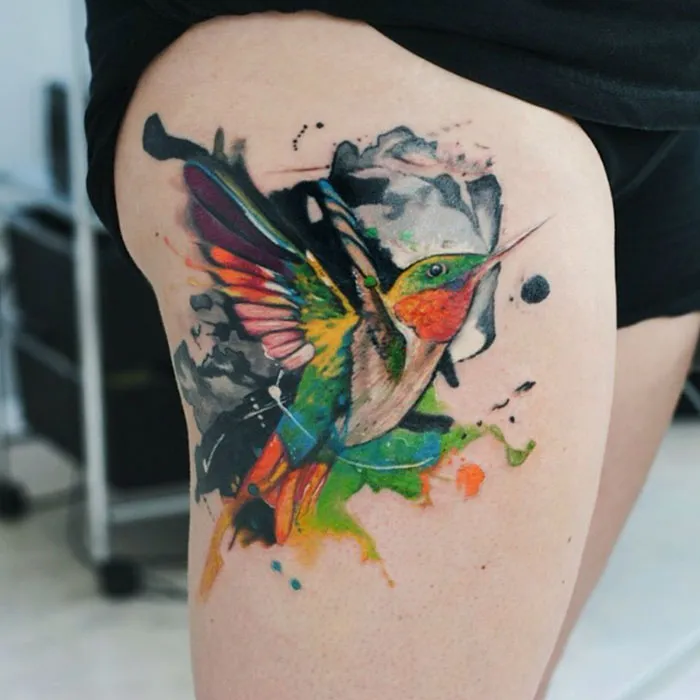 Colorful small bird tattoo on leg, displaying vibrant hues of green, orange, and pink.