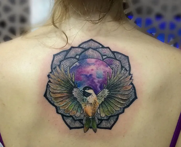 Colorful small bird tattoo on back with geometric patterns.