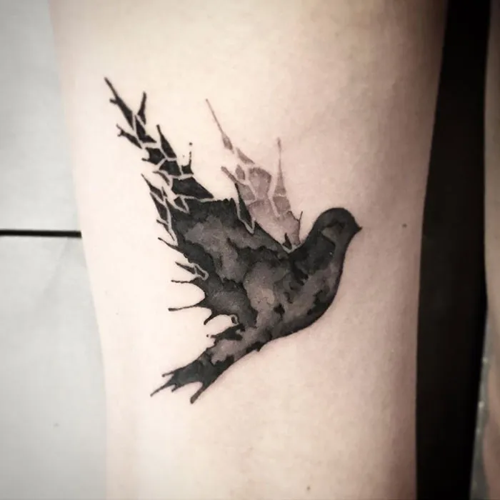 Unique small bird tattoo with artistic black shading on skin.