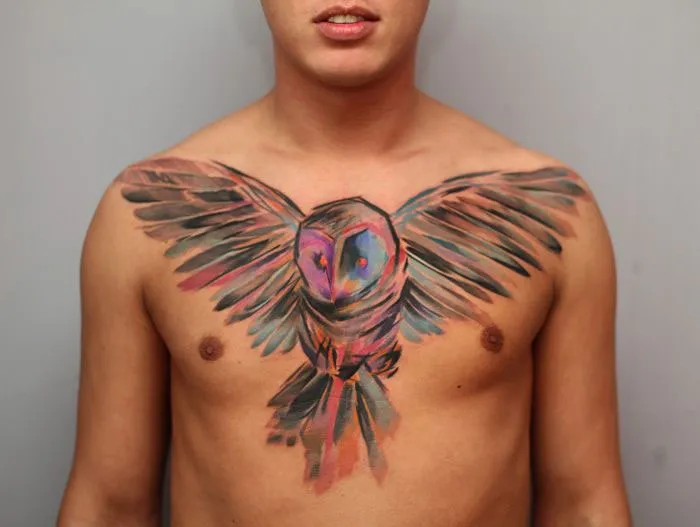 Colorful small bird tattoo on a man's chest, showcasing vibrant ink artistry.