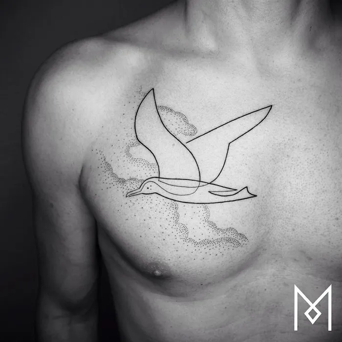 Minimalistic small bird tattoo on chest, featuring sleek line art and dotted clouds.