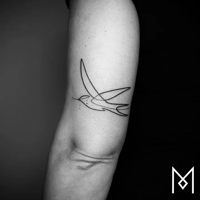 Minimalist small bird tattoo on forearm, showcasing unique design elements in black ink.
