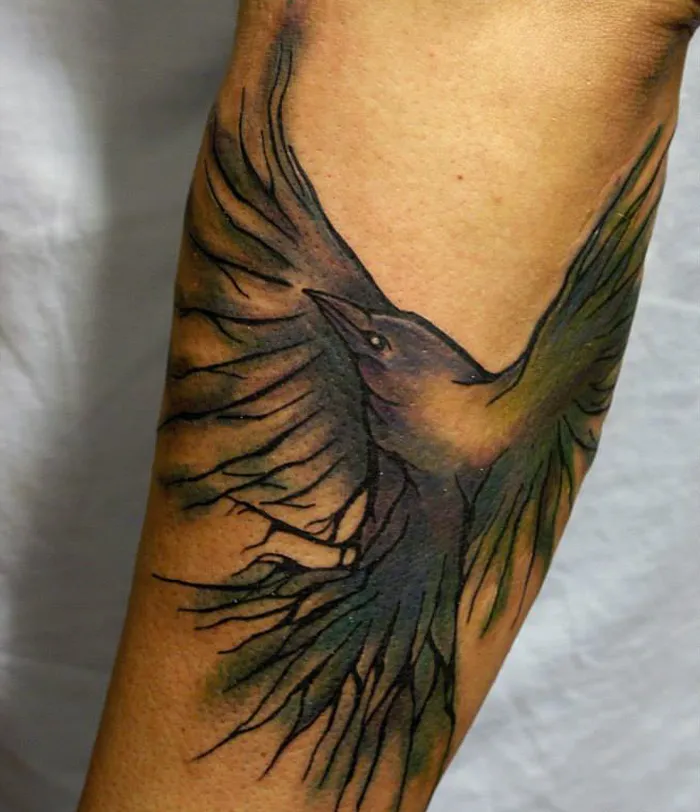 Small bird tattoo on forearm with detailed wing design, black and green hues.
