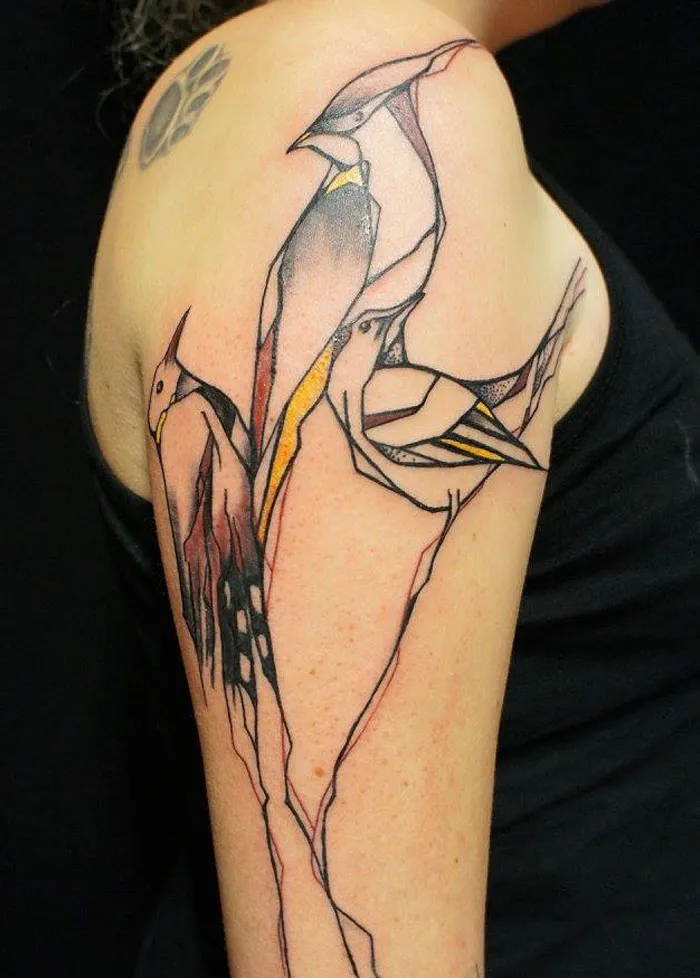 Abstract small bird tattoo on shoulder with geometric lines and muted colors.