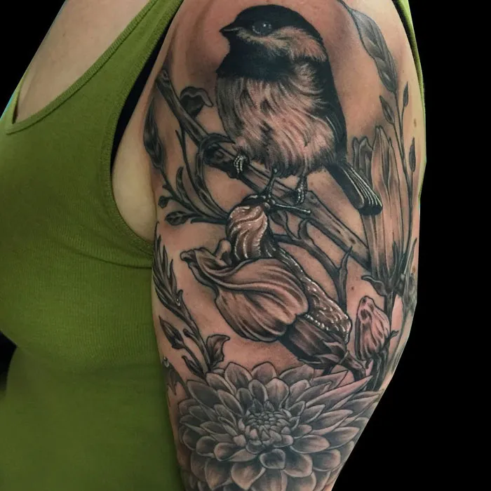 Arm tattoo featuring a detailed small bird perched on flowers and branches in black ink.
