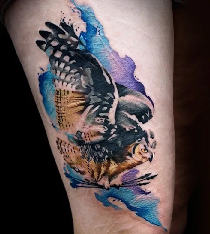 Watercolor style small bird tattoo with vibrant blue and purple accents on a person's arm.