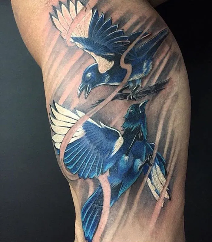 Two vibrant small bird tattoos with blue and white feathers, newly inked on arm.