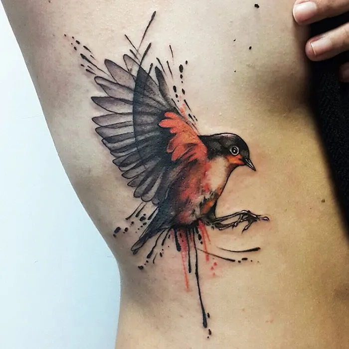 Unique small bird tattoo with vivid colors and artistic splatter design on the side of the body.