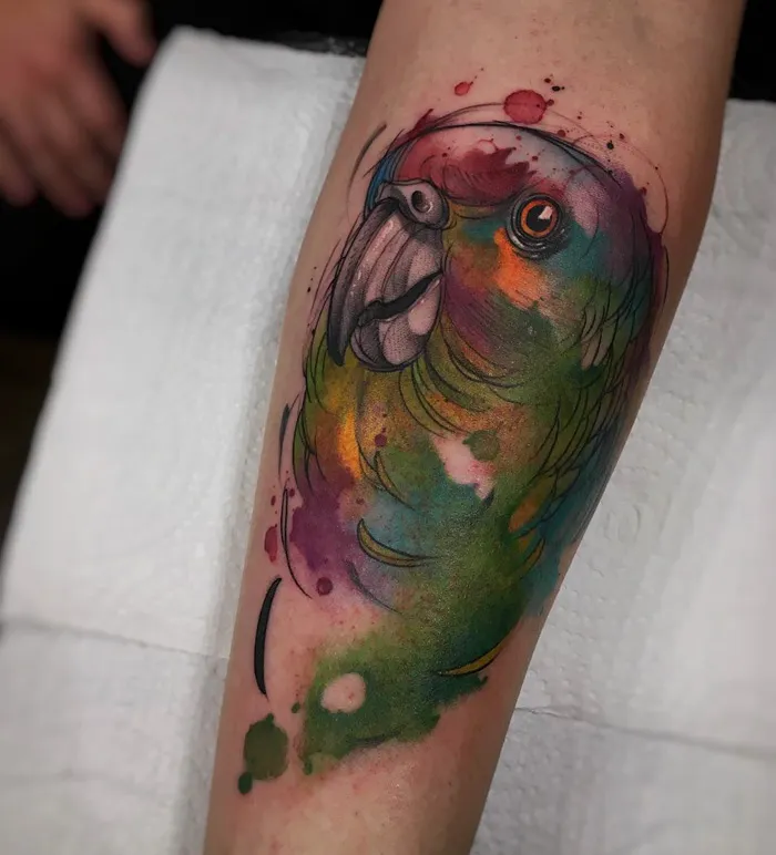 Colorful small bird tattoo with watercolor effect on arm.
