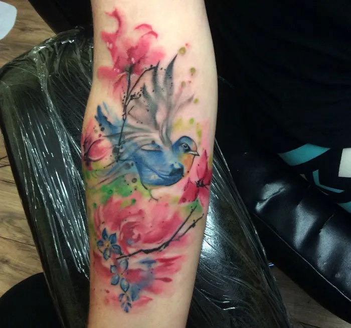 Colorful small bird tattoo with watercolor effect on arm.