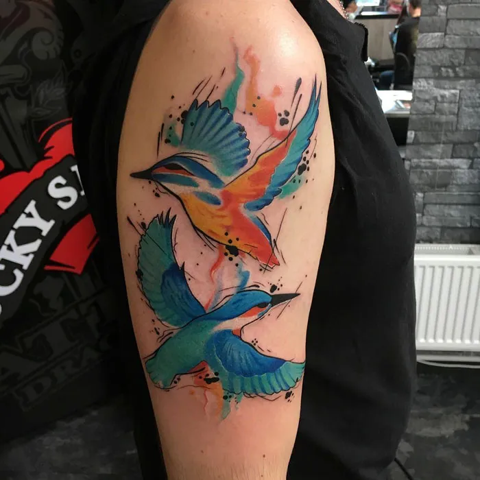 Colorful small bird tattoos on arm, featuring vibrant blues and oranges, creating a striking artistic masterpiece.